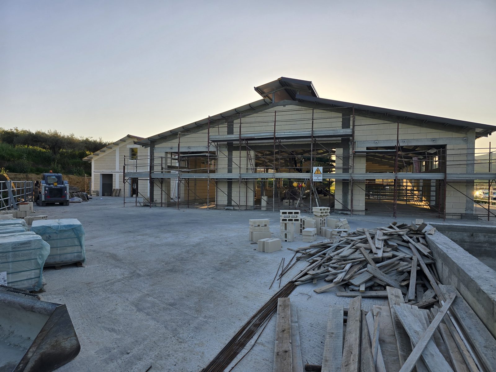 Piazzale di cantiere al tramonto davanti al capannone agricolo, materiale da costruzione in primo piano