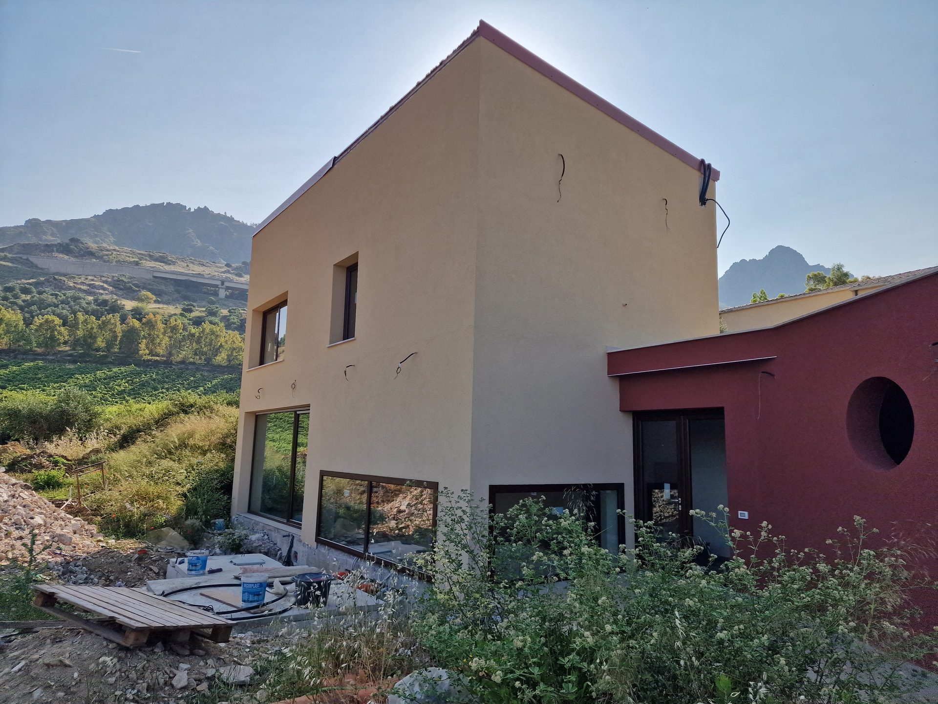 Centro benessere in costruzione su collina, volumi in intonaco beige e volume rosso